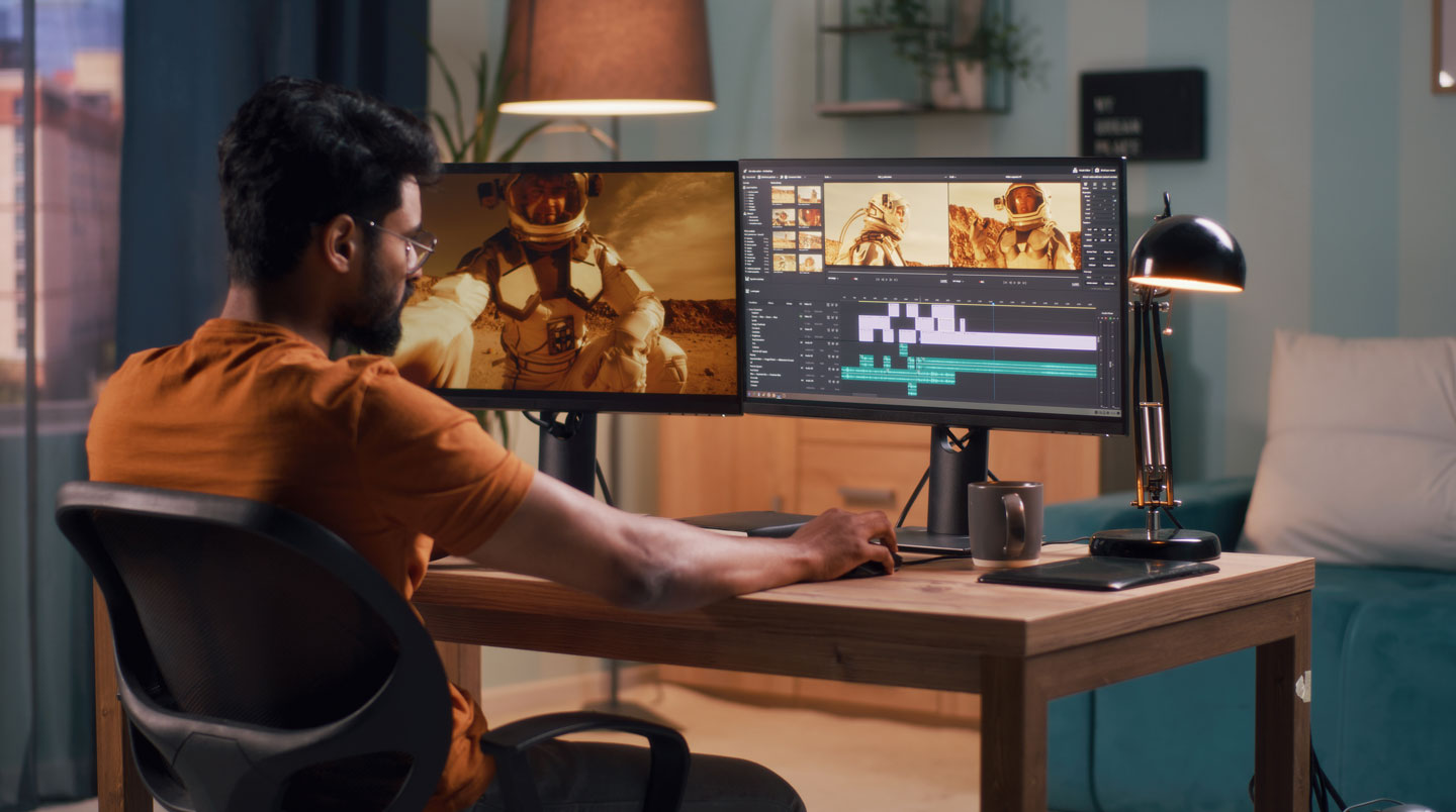 Nahaufnahme einer Hand, die eine Computermaus bedient, im Hintergrund ist ein unscharfer Videobearbeitungs-Bildschirm erkennbar